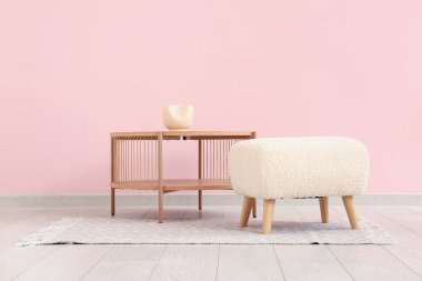 Ahşap sehpa ve pembe duvarın yanındaki puf.