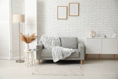 Aydınlık oturma odasının içinde şık bir halı ve gri kanepe var.