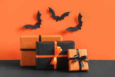 Cadılar Bayramı kutlaması için kağıt sopalarla hediye kutuları turuncu duvarın yanındaki siyah masada.