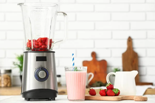 Modern blender and glass of tasty strawberry smoothie on table in kitchen