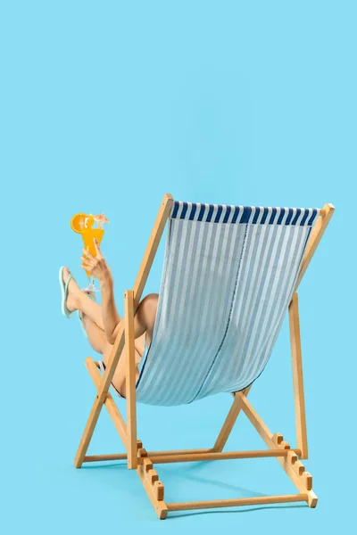 Beautiful woman with cocktail relaxing on sun lounger against blue background