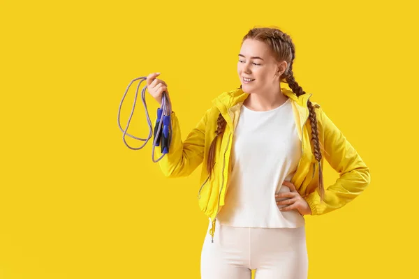 Sporty young woman with skipping rope on yellow background