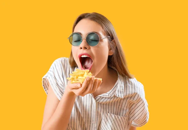 黄色の背景にフライドポテトを食べるサングラスの美しい若い女性 — ストック写真