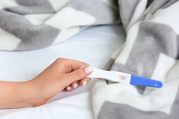 stock image Female hand with positive pregnancy test and plaid on bed, closeup