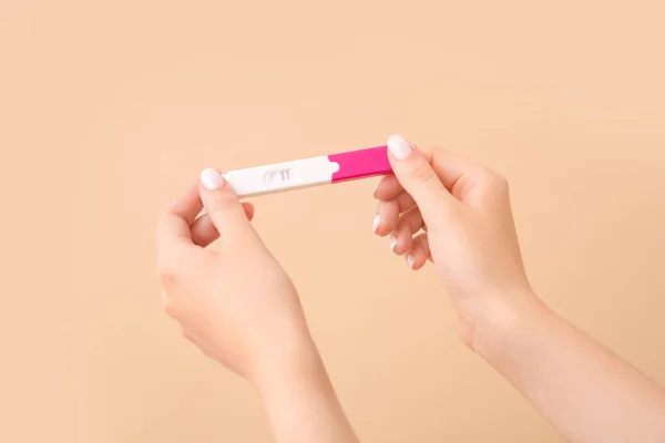 Female hands with positive pregnancy test on color background
