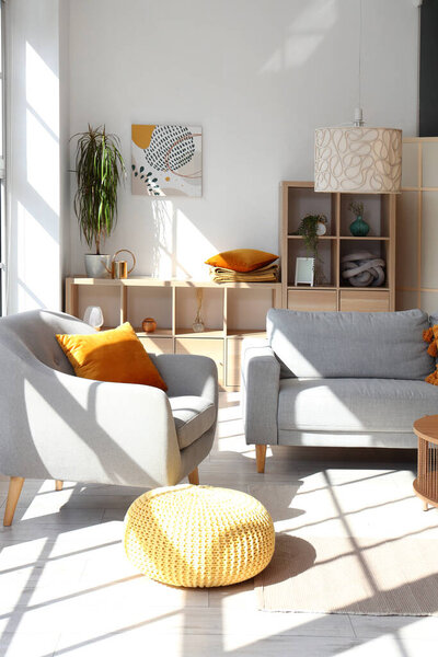 Интерьер светлой гостиной с серым диваном, креслом и пуфом