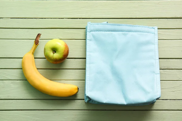 Lunch box bag with banana and apple on green wooden background