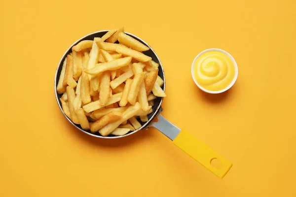 Frying pan with golden french fries and cheese sauce on orange background