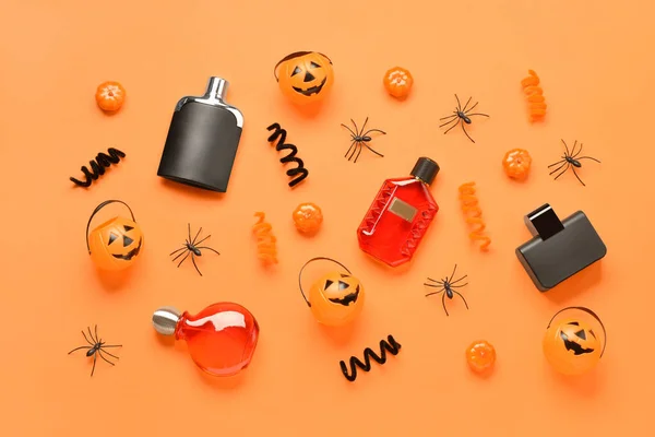Bottles of elegant perfume with Halloween decorations on orange background