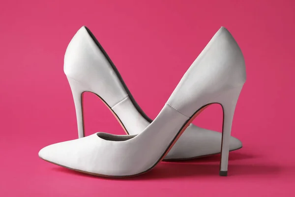 Stylish white high heels on pink background