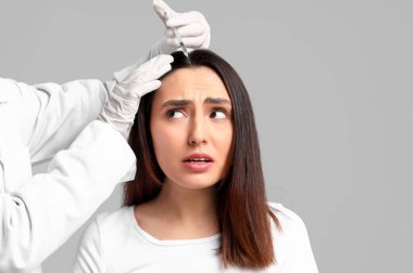 Saç dökülmesi sorunu olan bir kadın gri arka planda iğne oluyor.