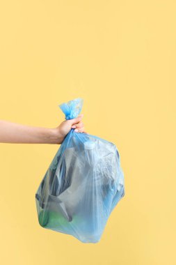 Sarı arka planda çöp torbası tutan kadın.