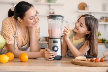 Küçük kız ve annesi mutfakta blender ile smoothie yapıyorlar.