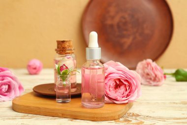 Gül özlü kozmetik yağı şişeleri ve açık ahşap masa üzerinde çiçekler.