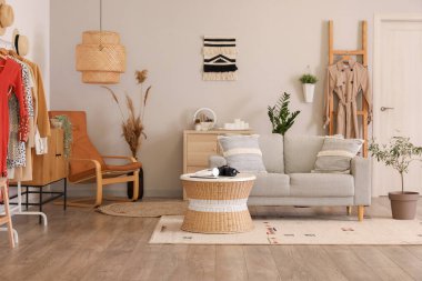 Gri kanepe, masa ve kıyafetlerle aydınlık oturma odasının içinde.