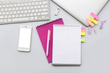 Gri arkaplanda klavyesi, telefonu ve kırtasiyesi olan dizüstü bilgisayar