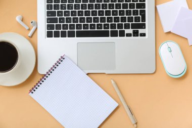 Kulaklıklı laptop, turuncu arka planda bir fincan kahve ve kırtasiye malzemesi.