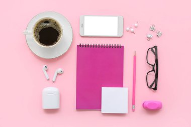 Gözlüklü bir fincan kahve, pembe arka planda cihazlar ve kırtasiye malzemesi.