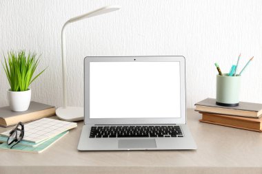 Modern dizüstü bilgisayarı, kitapları ve bej masadaki bitki örtüsüyle rahat bir iş yeri.