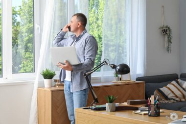 Ofiste cep telefonuyla konuşan, dizüstü bilgisayarı olan yetişkin bir erkek serbest yazar.