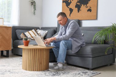 Evde kanepede dizüstü bilgisayarla çalışan olgun bir erkek serbest yazar.