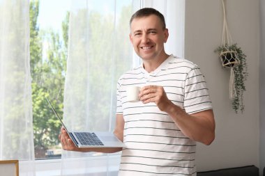 Evde dizüstü bilgisayarı ve bir fincan kahvesi olan olgun bir serbest çalışan.