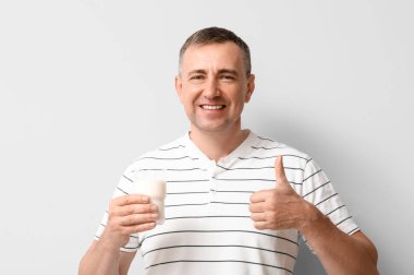 Beyaz arka planda baş parmağını gösteren bir bardak sütle olgun bir adam.