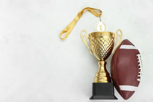Gold cup with first place medal and rugby ball on white background