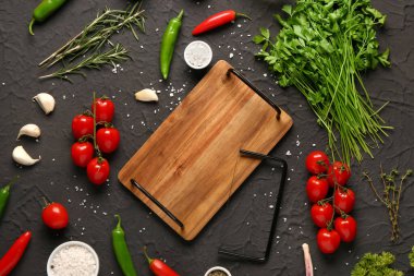 Ahşap mutfak tahtası, taze sebzeler, koyu arkaplanda otlar ve baharatlar.