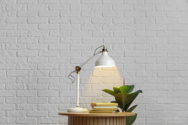 Parlayan lamba, kitaplar ve beyaz tuğla duvarın yanındaki çiçekli masa.