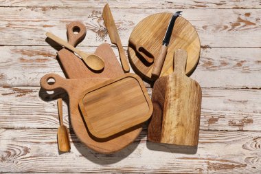 Açık ahşap arka planda kaşık ve bıçaklarla farklı kesme tahtaları.