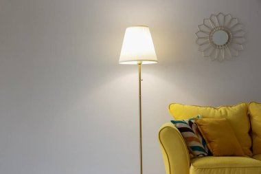 Parlayan lamba, yastıklı sarı kanepe ve beyaz duvarın yanındaki ayna.