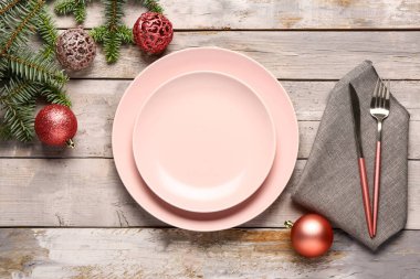 Pembe tabaklar, çatal bıçak takımı, Noel baloları ve gri ahşap arka planda köknar ağacı dalları olan şenlik masası.