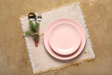 Pembe tabaklar, çatal bıçak takımı ve kahverengi arka planda köknar ağacı dalı olan Noel sofrası.