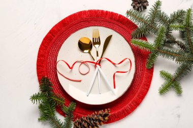 Altın çatal bıçak seti, köknar dalları ve beyaz arka planda çam kozalakları.