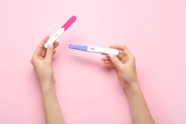 Pembe arka planda hamilelik testi olan kadın eller.