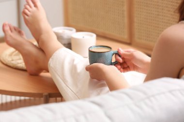 Evdeki kanepede bir fincan lezzetli kahveyle dinlenen kadın.