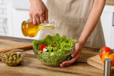 Mutfaktaki masada lezzetli salata ile zeytinyağı ekleyen bir kadın.
