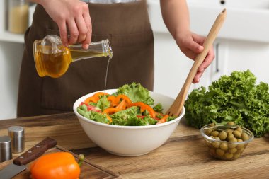 Mutfaktaki masada lezzetli salata ile zeytinyağı ekleyen bir kadın.