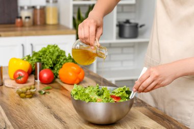 Mutfaktaki masada lezzetli salata ile zeytinyağı ekleyen bir kadın.