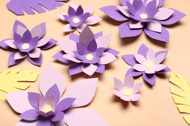 Bej arkaplanda yaprakları olan renkli origami çiçekleri