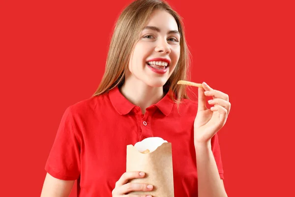 赤い背景にフランスのフライドポテトのパックを持つ美しい幸せな若い女性 — ストック写真