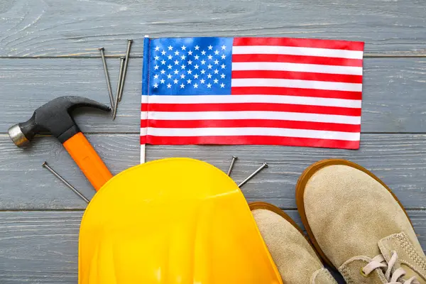 stock image Hardhat, boots, hammer and USA flag on grey wooden background. Labor Day celebration