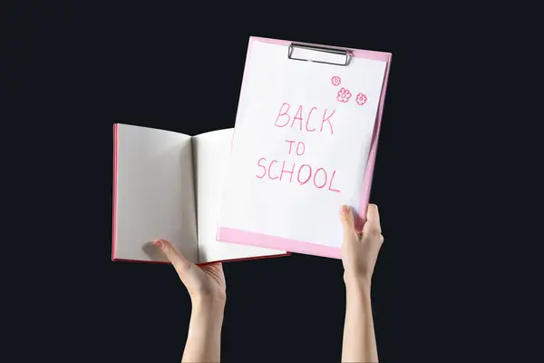 手握带文字的笔记本的女性 在黑色背景下返回学校 — 图库照片
