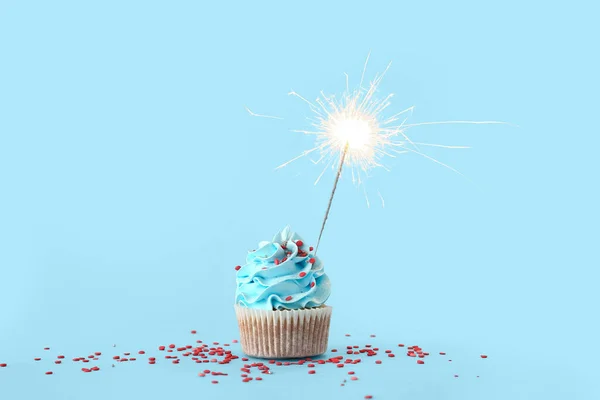 Tasty birthday cupcake with sparkler on blue background