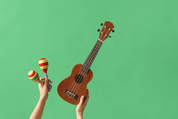 Female hands holding maracas and ukulele on green background