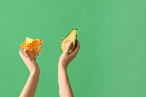 Female hands holding nachos and avocado on green background