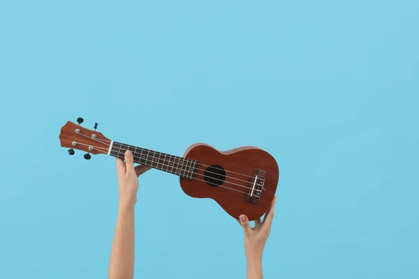 Female hands holding ukulele on blue background