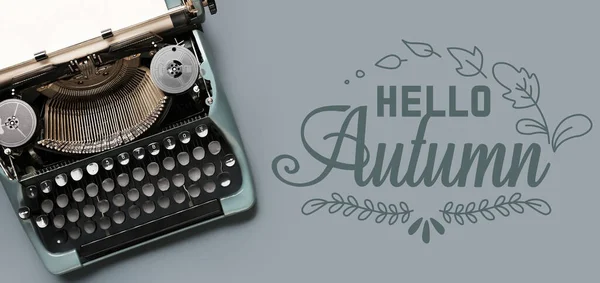 Vintage typewriter with text HELLO AUTUMN on grey background