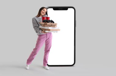 Büyük akıllı telefon ve arka planda bir sürü pizza kutusu, içki ve oyun pedi olan güzel genç bir kadın.